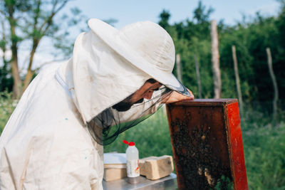 Side view of beekeeper examining beehive on land