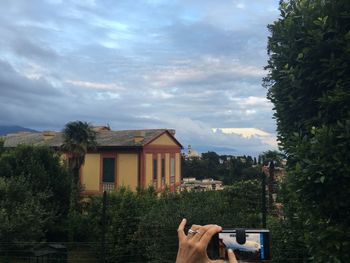 Cropped image of hand photographing house and cloudy sky with smart phone