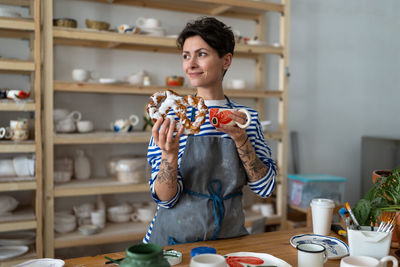 Happy female pottery master taking coffee break in ceramics studio, having lunch in clay studio