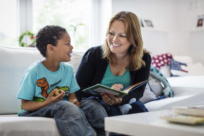 Happy mother and son looking at each other while reading picture book on sofa