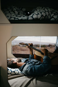 Man holding guitar while lying down on bed at home