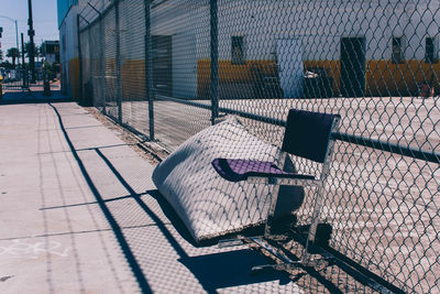 Shadow of man on empty bench by chainlink fence