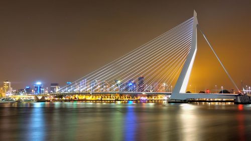 Erasmus bridge over river by illuminated city at night