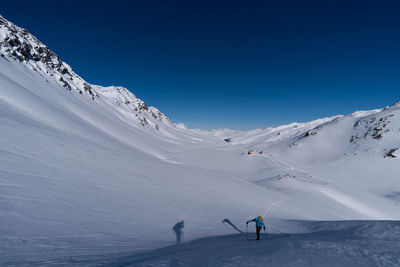 Person hiking on snowcapped mountains against clear blue sky