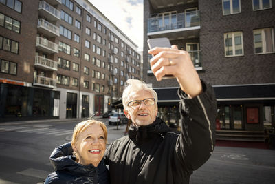 Senior couple taking selfie through smart phone while standing in city
