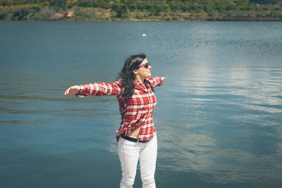 Beautiful young woman with arms outstretched standing against lake