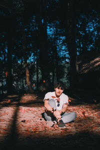 Young man sitting under leaves in mid-air against trees in forest