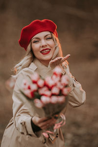 Portrait of smiling young woman blowing kiss while holding bouquet outdoors