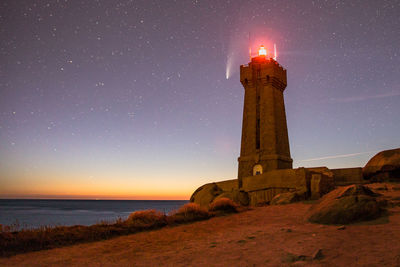 Lighthouse by sea against sky at night