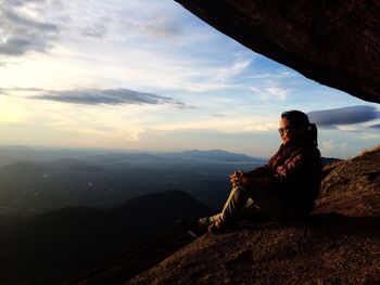 Full length of woman enjoying view from rock against sky during sunset