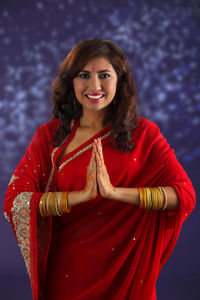 Portrait of beautiful indian woman in red sari greeting against purple background