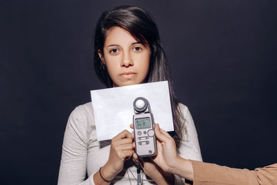 Portrait of a young woman holding camera against black background