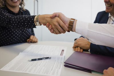 Mature businesswoman shaking hands with colleague sitting at desk in office