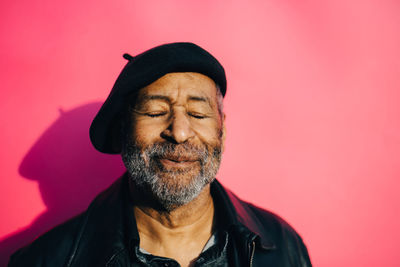 Smiling senior man with eyes closed against pink background