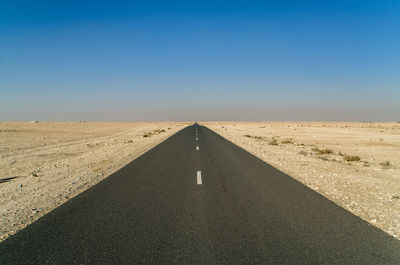 Road leading towards desert against clear sky