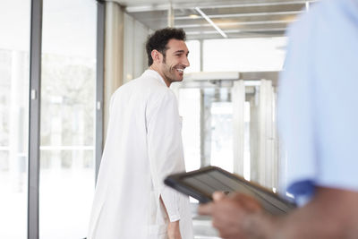 Smiling young doctor walking while male nurse holding digital tablet at lobby in hospital