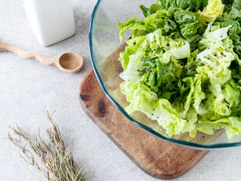 Bowl with freshly washed lettuce on wet white wooden background