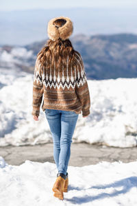 Rear view of woman walking on snow covered land during winter