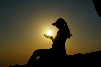 Silhouette woman sitting on rock against sky during sunset