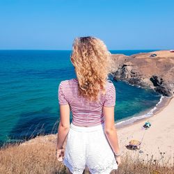 Rear view of woman standing at beach while looking at horizon