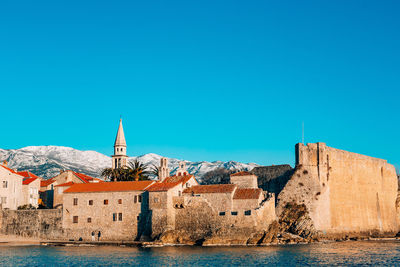 Buildings by sea against blue sky