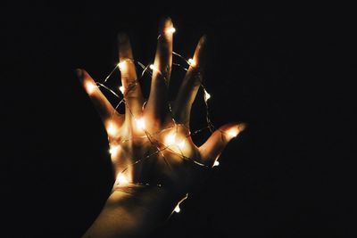 Cropped image of hand with illuminated christmas light against black background