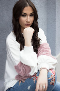 Portrait of beautiful woman with hand on chin sitting against wall