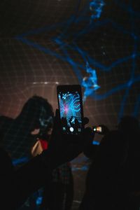 Close-up of silhouette hand holding illuminated smart phone at night
