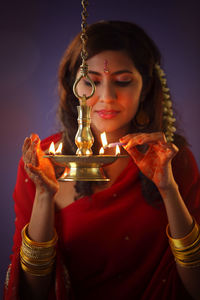Beautiful indian woman in red sari lighting diya during diwali