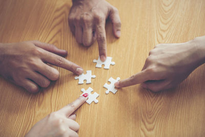 High angle view of people holding jigsaw piece on table