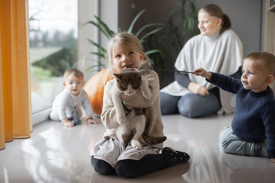 Mother with her three children playing with a cat on the floor at home