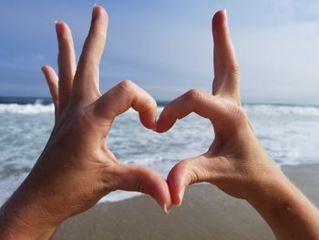 Close-up of hands over sea against sky