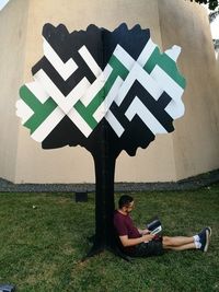 Man reading book while sitting against artificial tree