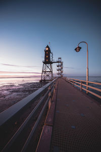 Railroad tracks by sea against clear sky during sunset