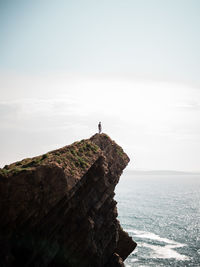 Man standing on rock by sea against sky