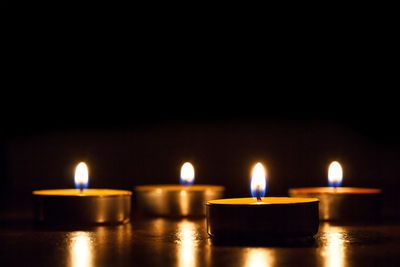Close-up of illuminated tea light candles on table against black background