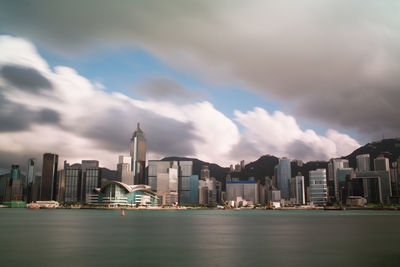 Hong kong victoria harbour buildings in city against cloudy sky