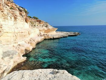 Rock formations by sea against blue sky