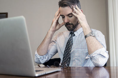 Tensed businessman using laptop at desk in office