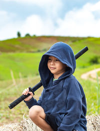 Thoughtful boy holding sword while sitting on landscape