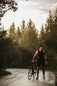 Young man standing by bicycle on road