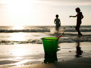 Close-up of bucket on beach with kids playing at beach