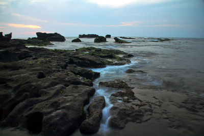Rocks on beach against sky during sunset