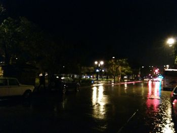 Illuminated city by river against sky at night