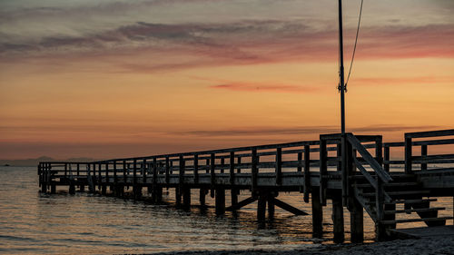 Pier over sea against orange sky