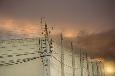 Low angle view of electricity pylon against sky during sunset