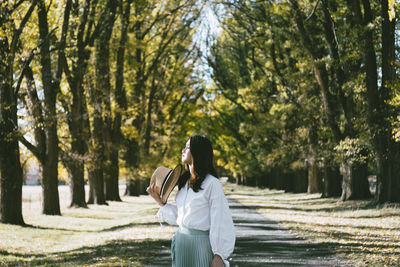 Young woman standing on road against trees in park during sunny day