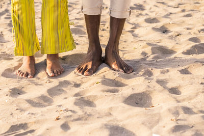 Low section of men and woman standing on sand