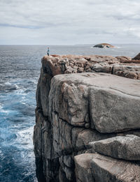 Distant view of woman standing on cliff by sea