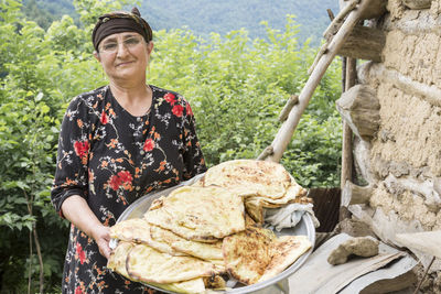 Portrait of woman holding breads in plate against plants